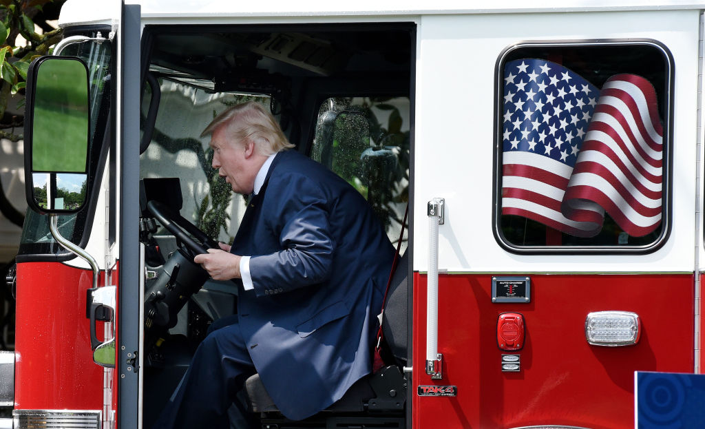 President Donald Trump sits in a fire truck at the White House and pretends to drive it