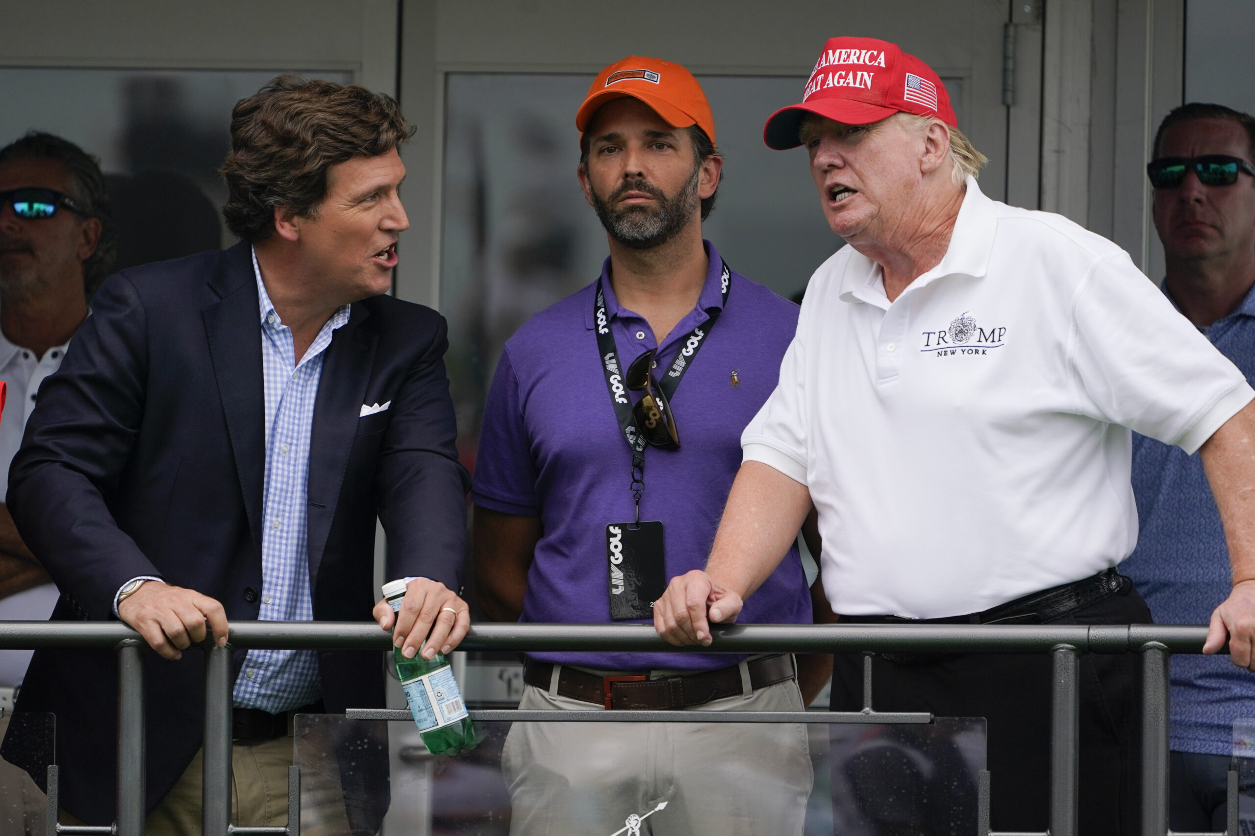 Former President Donald Trump, right, talks with Donald Trump Jr., center, and Tucker Carlson