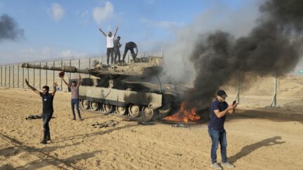FILE - Palestinians celebrate by a destroyed Israeli tank at the Gaza Strip fence east of Khan Younis Saturday, Oct. 7, 2023.