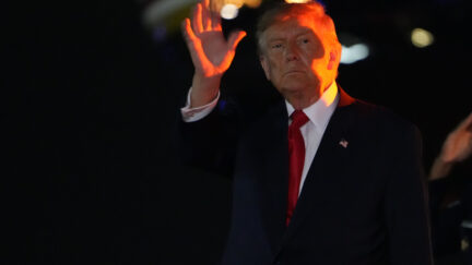 trump waves in the nighttime with a red light shining on him
